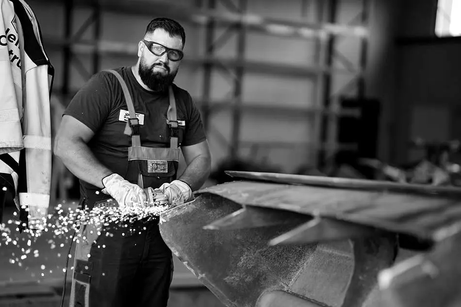 Muncitor Nello Construct care șlefuiește o piesă metalică, cu scântei